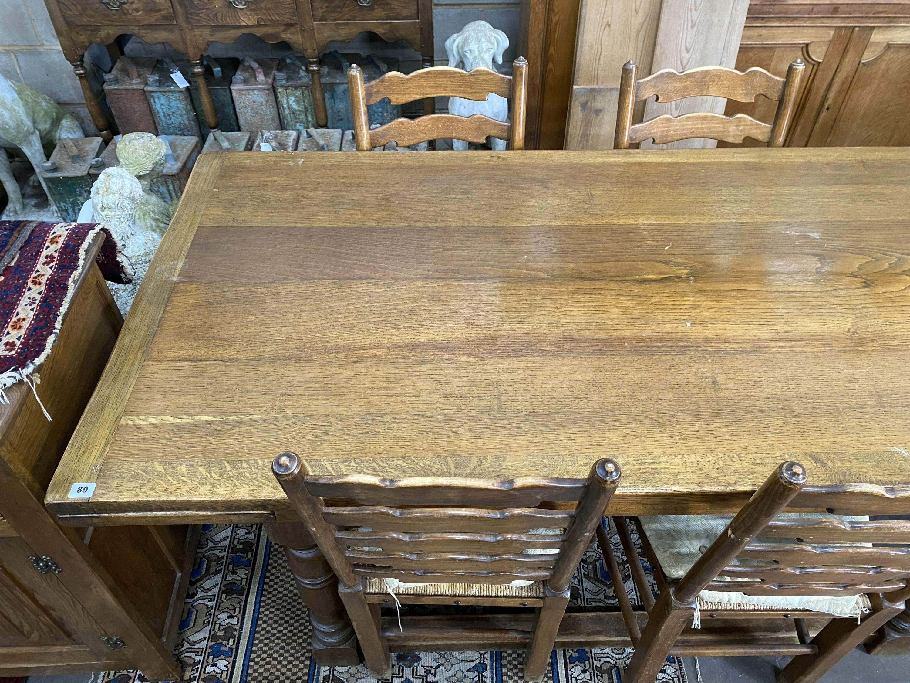 An 18th century style oak dining suite comprising extending draw leaf refectory table, 243cm extended, width 90cm, height 76cm, six rush seat ladder back chairs, two with arms and a linenfold moulded sideboard